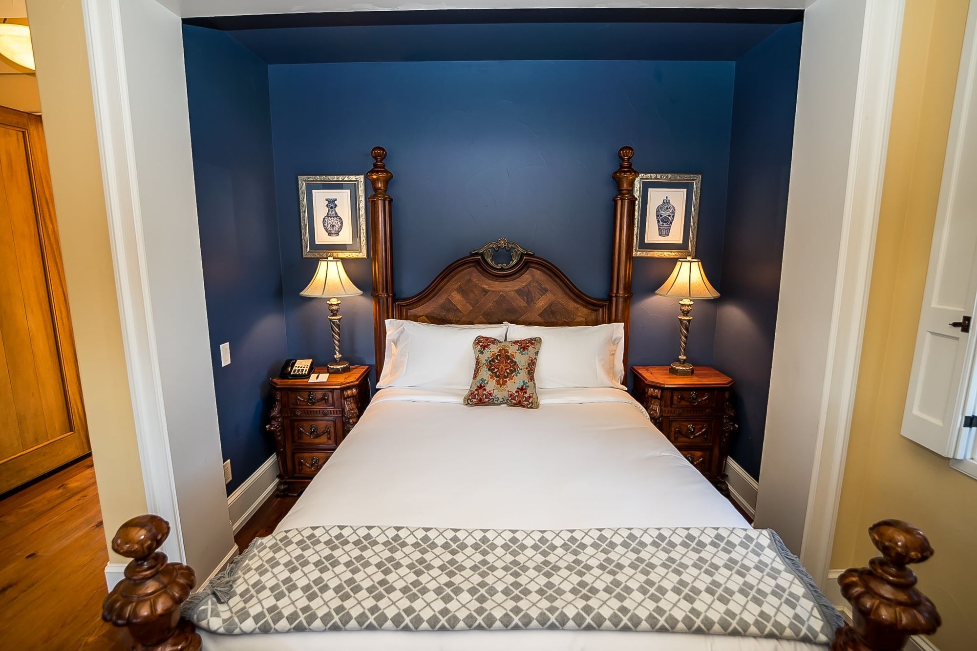 Bed made with white sheets with an accent pillow set in a niche painted dark blue