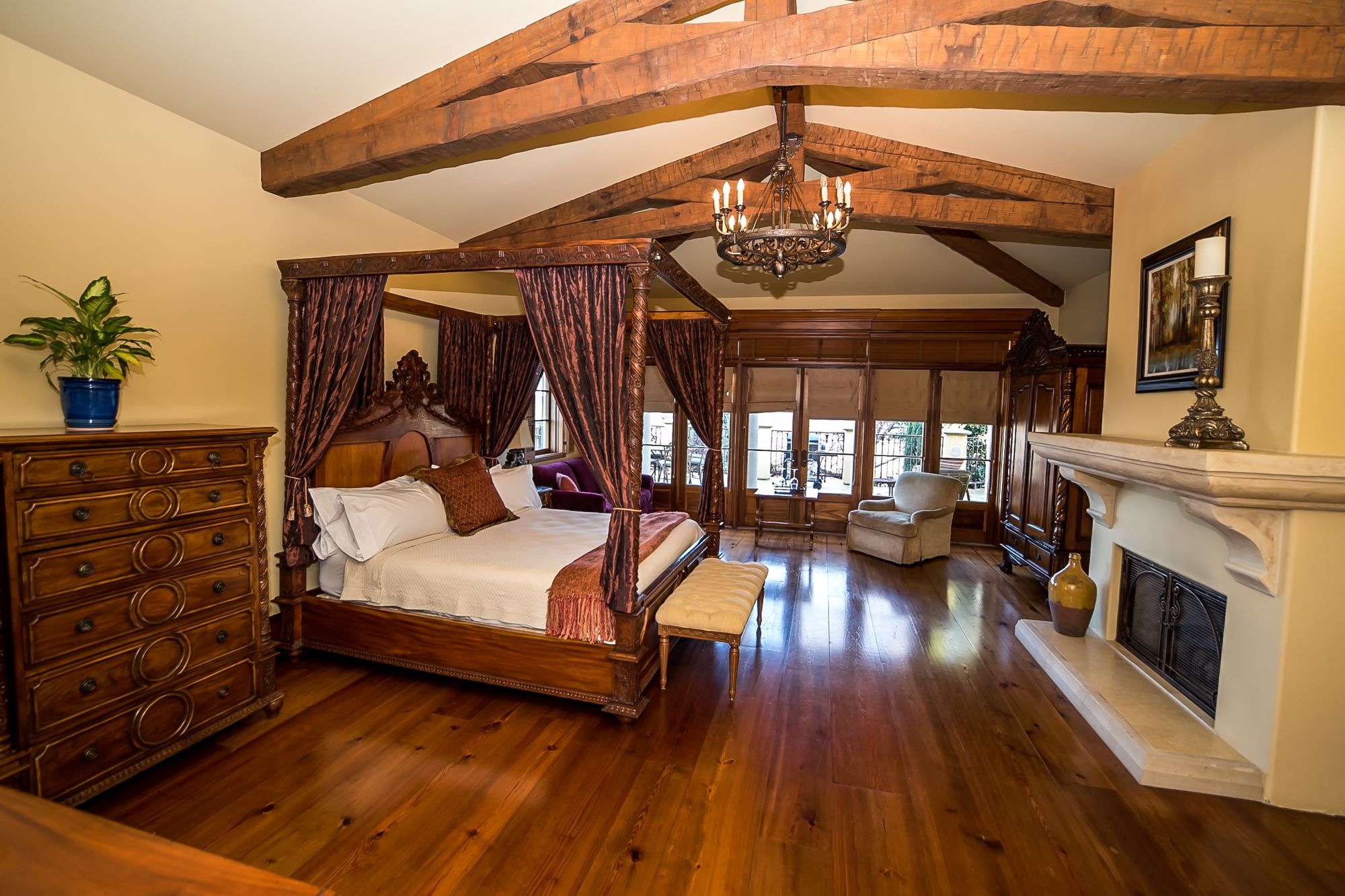 Big wooden rafters with canopy bed to the left and chest of drawers and decorative fireplace to the left