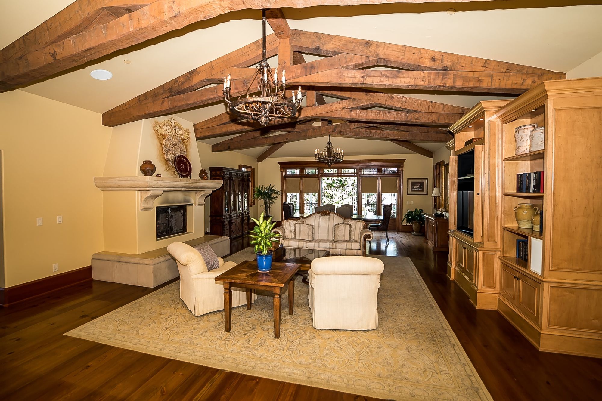 Sitting room with decorative fireplace, television cabinet, chandeliers suspended from the ceiling with rafters